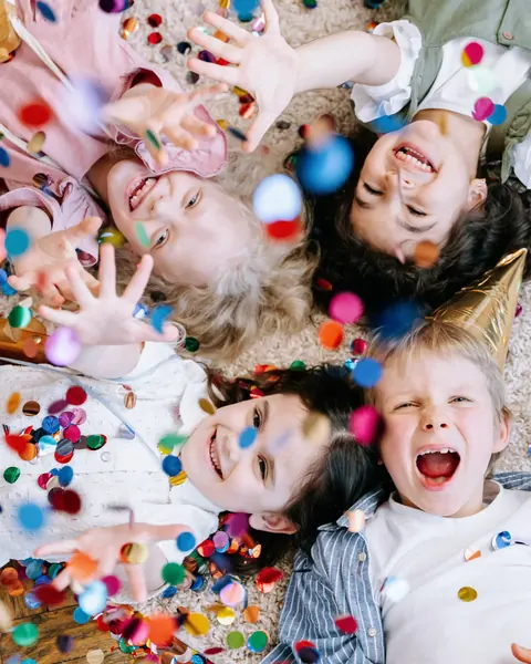 Lachende Kinder liegen im Kreis auf einem Boden voller Konfetti